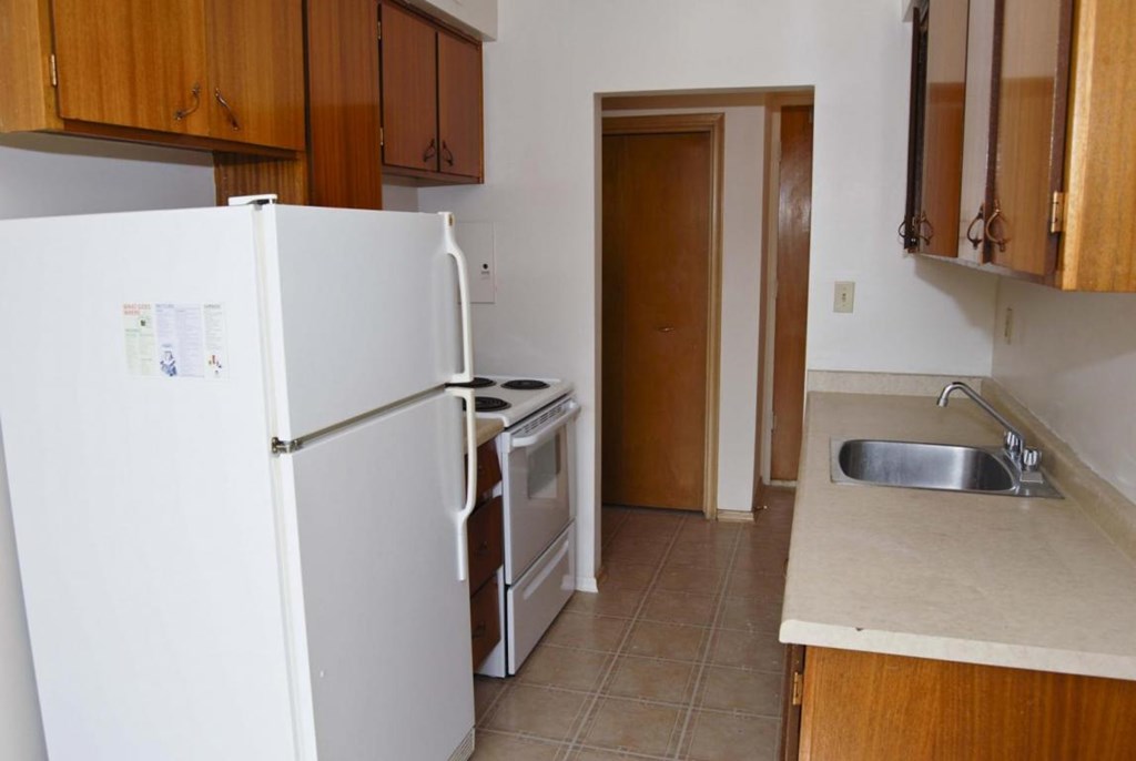 A kitchen with a white fridge, wooden cabinets, and a sink.