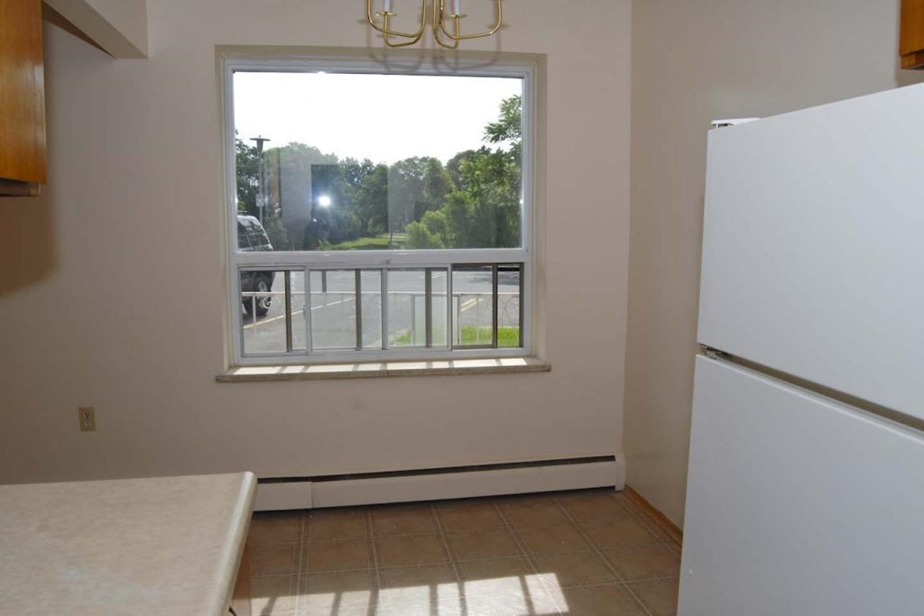 A white refrigerator sits in a kitchen next to a window.