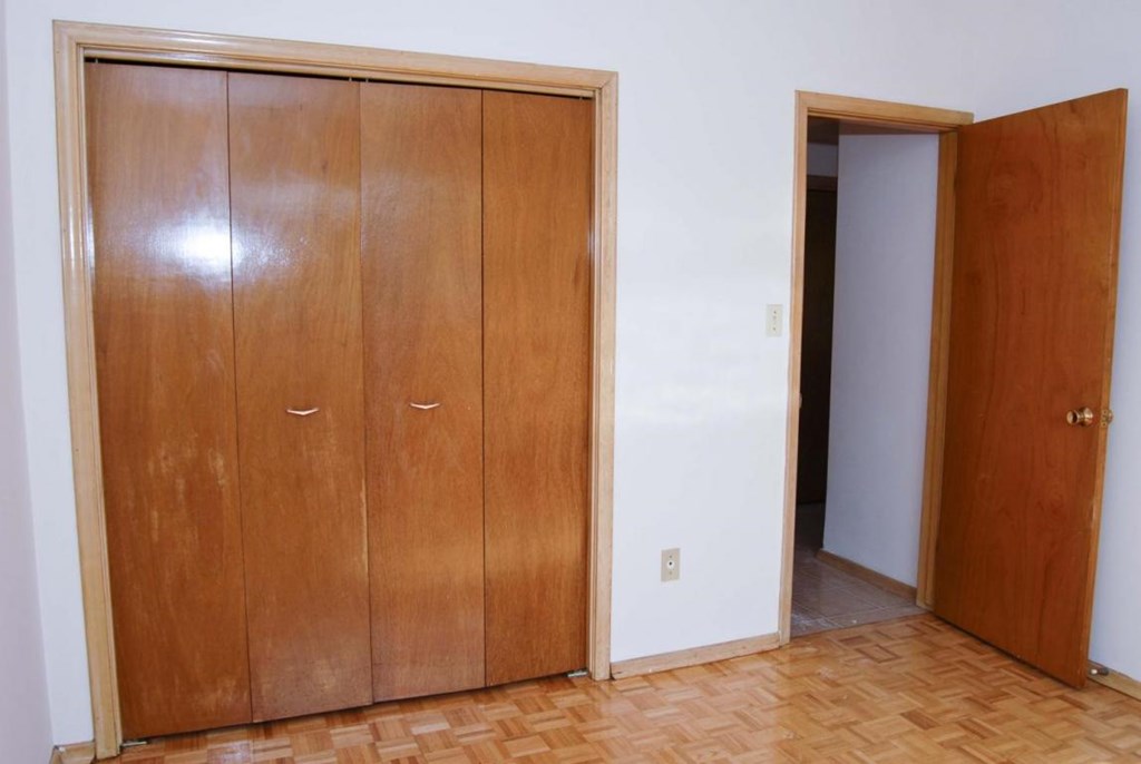 A room with a wooden floor and a large wooden wardrobe with two doors and a smaller door.