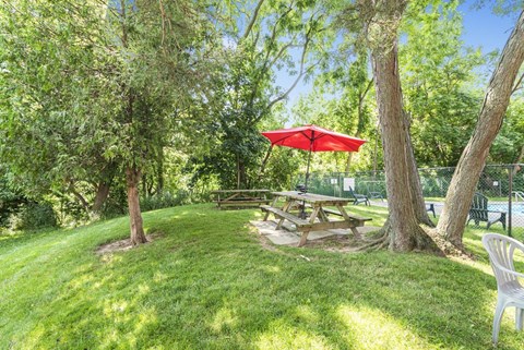 A picnic table is set up under a red umbrella in a grassy area.
