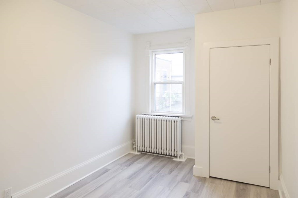 A room with a white door, a window with a white frame, and a white radiator on the floor.