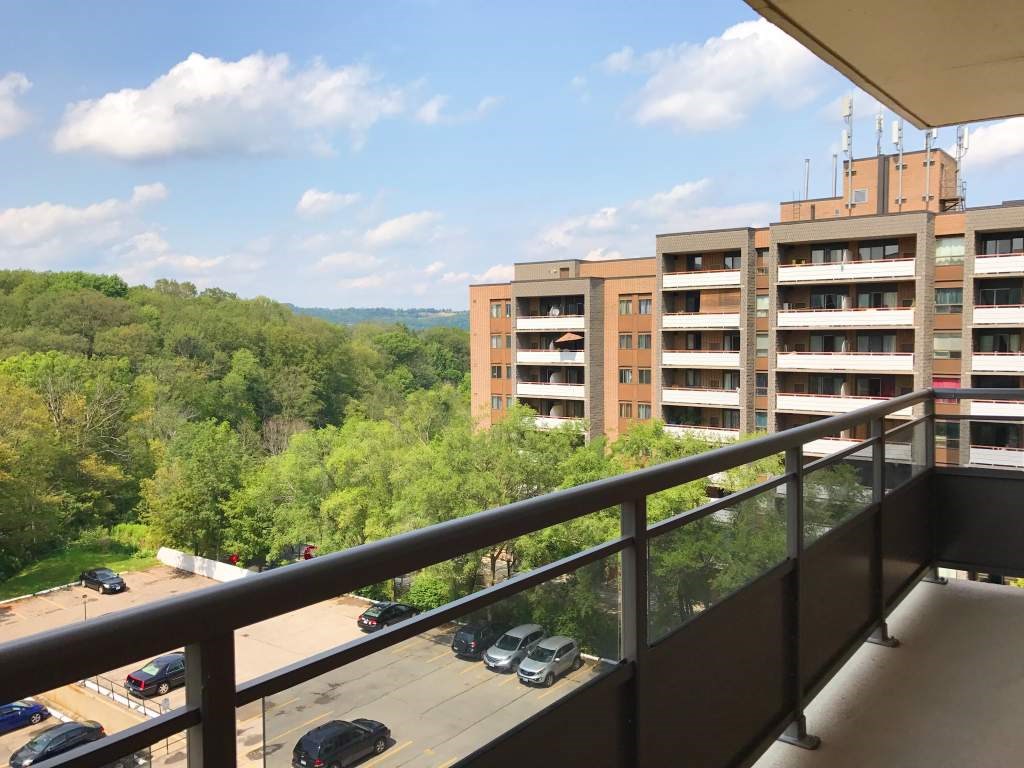 A balcony overlooks a parking lot and a wooded area.