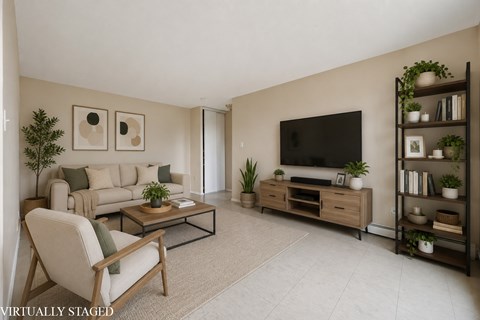 A living room with a white chair, a brown couch, a glass coffee table, a flat screen TV, and a bookshelf with plants.