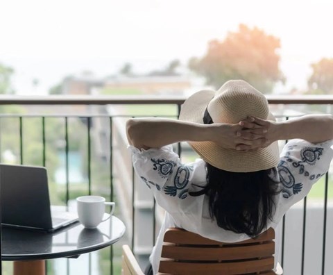 A woman in a hat is sitting on a chair with her back to the camera, looking out of a balcony.at Sylk Towers, Kitchener, ON N2A 1B1