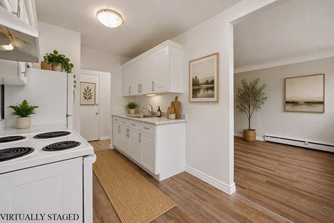 A white kitchen with a stove top oven and wooden floors.