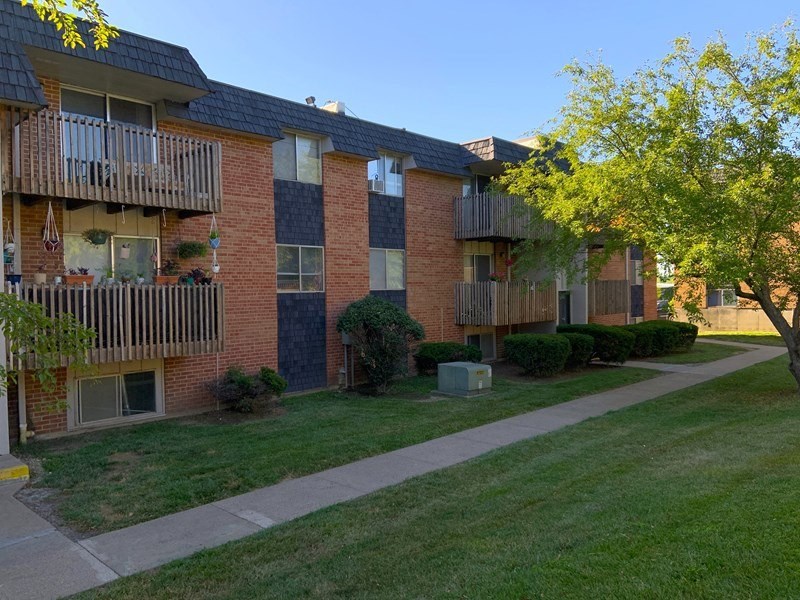 Apartment building with a green lawn, sidewalk, and tree in front.