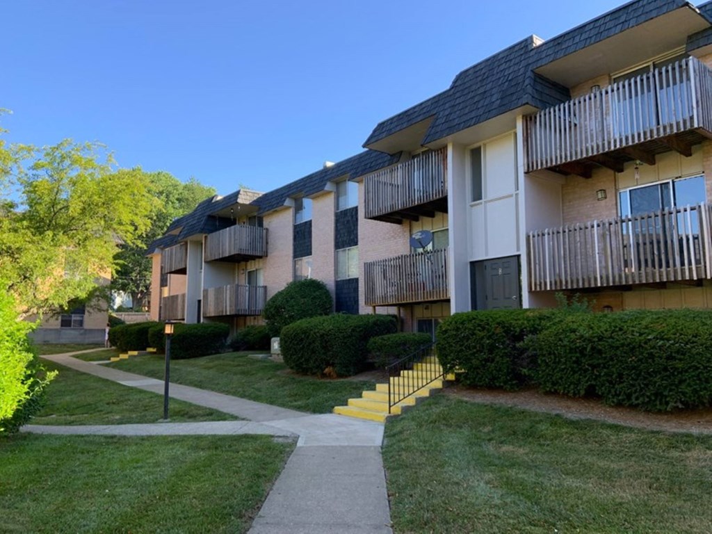 An apartment building with balconies and a walkway in front of it.