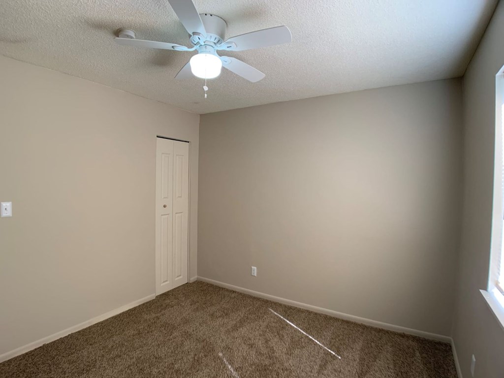 A room with a ceiling fan and carpeted floor.