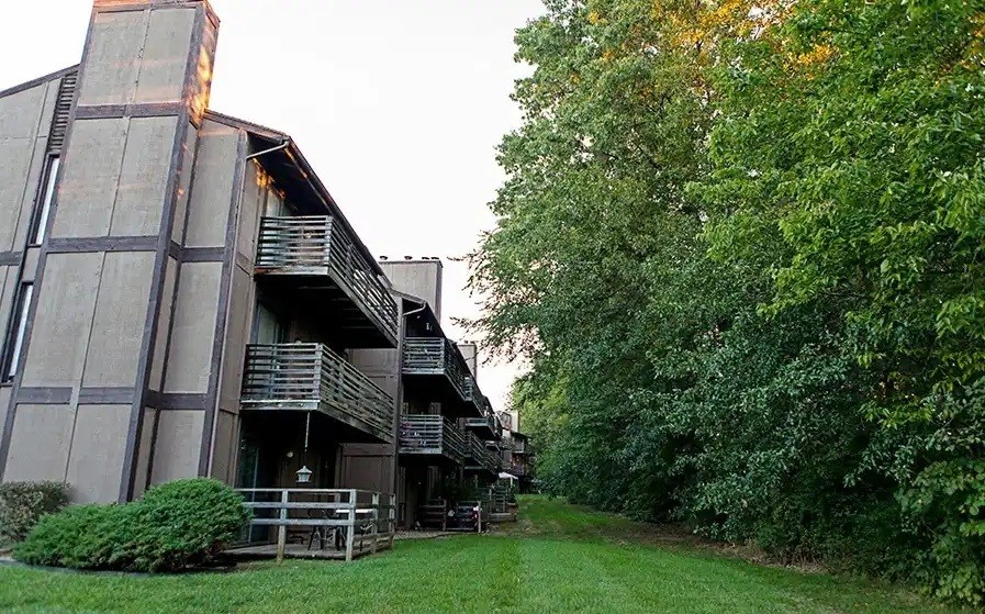 A building with a balcony and a green lawn with trees.