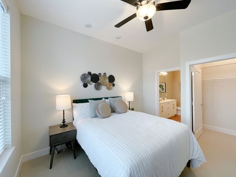 A bedroom with a bed, a ceiling fan, and a nightstand with a lamp.
