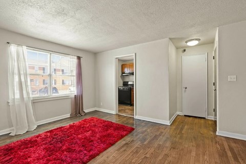 A room with a red rug on the floor and a window with curtains.