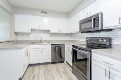 A kitchen with white cabinets and a black microwave.