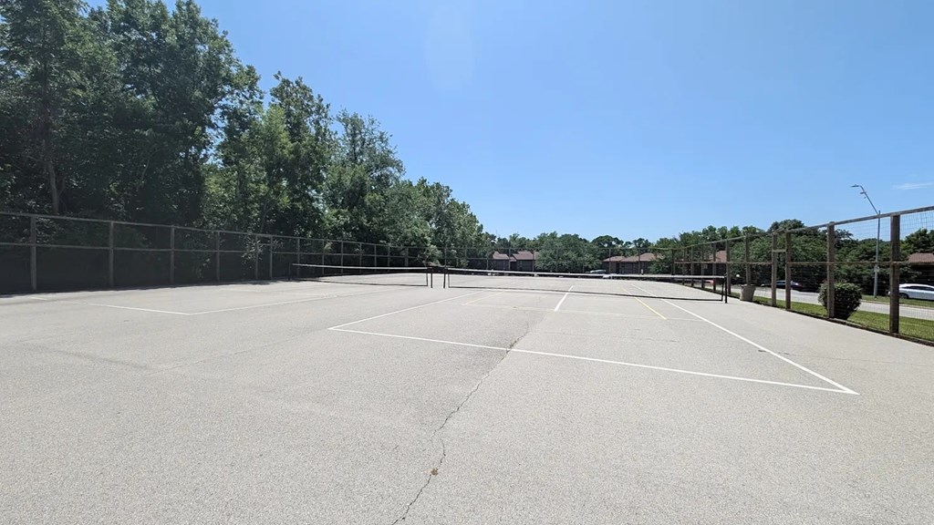 A tennis court surrounded by a fence and trees.