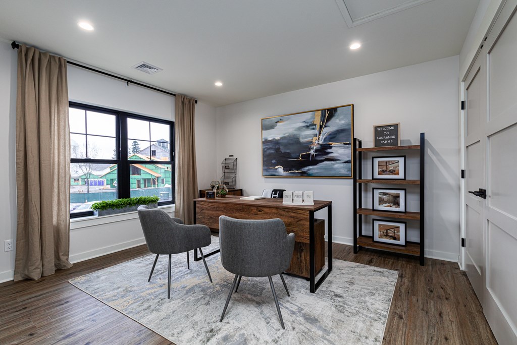 A room with a desk, chairs and a painting on the wall.
