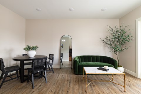 A living room with a green sofa, a round table with chairs, and a coffee table with a plant on it.