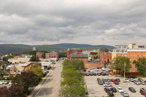 A parking lot with cars and a road in the foreground with buildings and trees in the background.