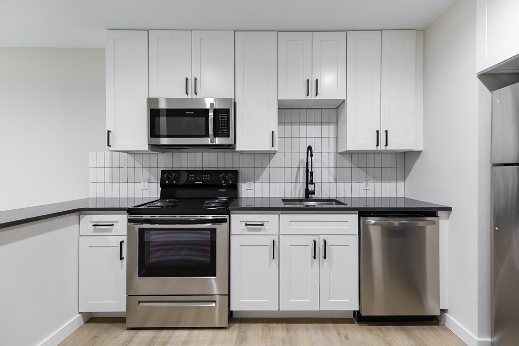 A kitchen with white cabinets and black countertops.