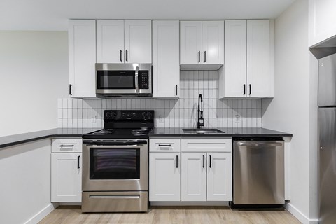 A kitchen with white cabinets and black countertops.