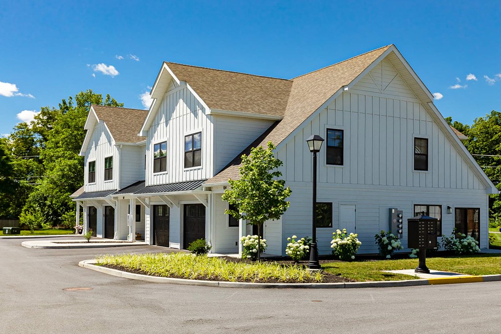 A white barn-style building with a brown roof and a porch.