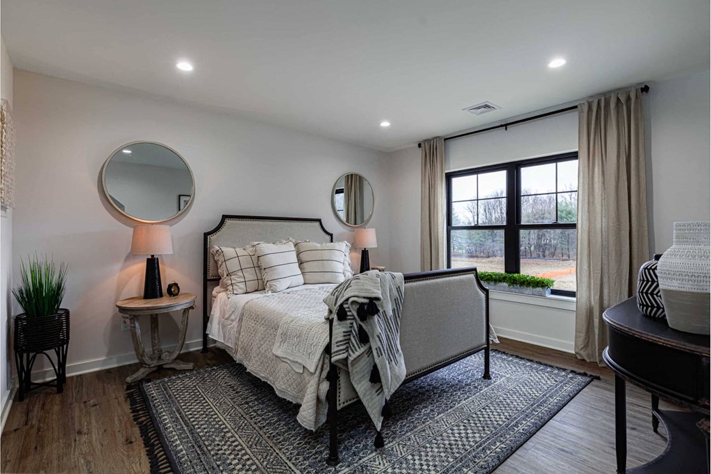 A bedroom with a bed, a side table with a lamp, and a window with a view of trees.