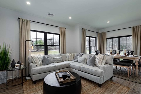 A modern living room with a grey sofa, a coffee table, and a dining table set up.