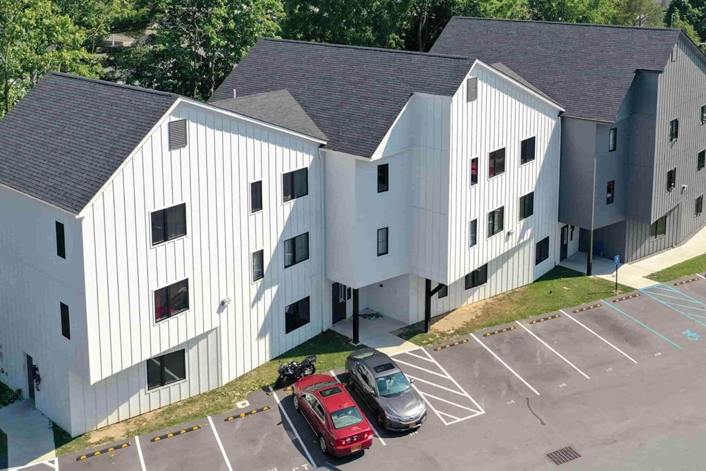 A red car is parked in a parking lot in front of a white building.