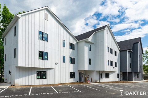 A modern white building with a black roof and a parking lot in front.