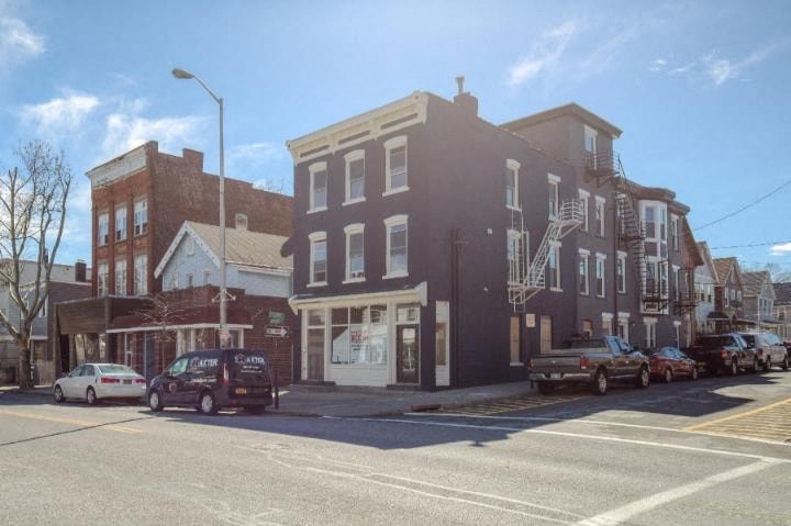 A street view of a city with cars parked on the side of the road and buildings in the background.