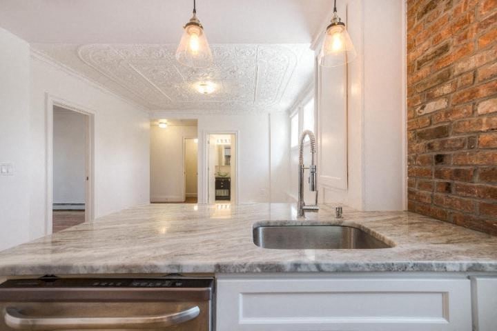 A kitchen with a marble countertop and a brick wall.
