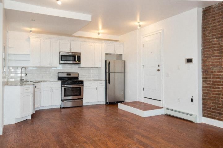A kitchen with white cabinets and a brick wall.