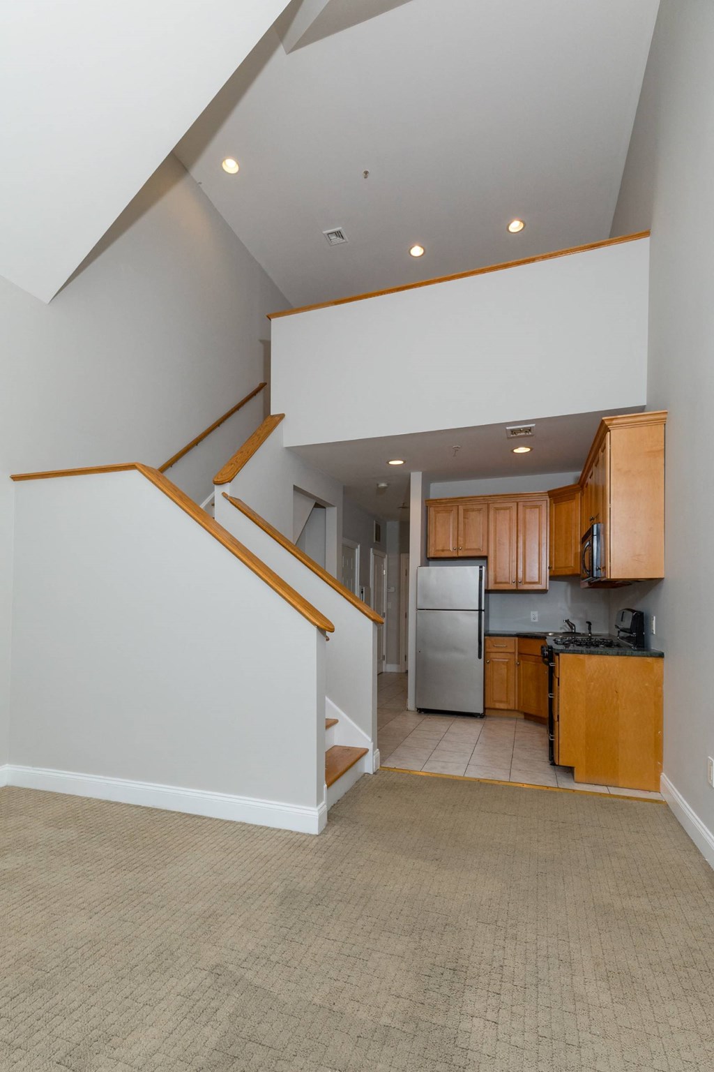 A kitchen with a refrigerator, microwave, and oven is visible from the stairs.