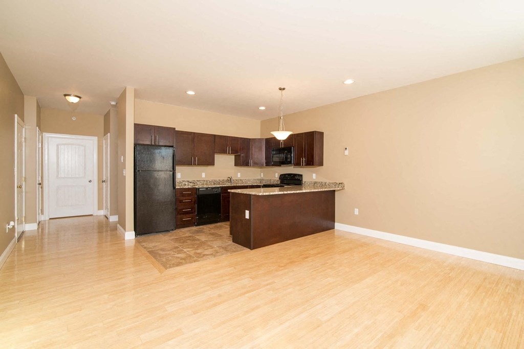 A kitchen with a black refrigerator and wooden floors.