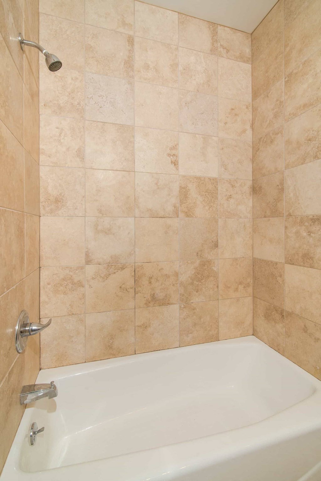 A white bathtub with a shower head and a tile wall.