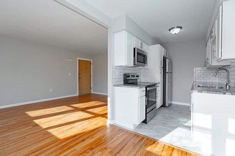 A kitchen with white cabinets and appliances, a wooden floor, and a door to another room.