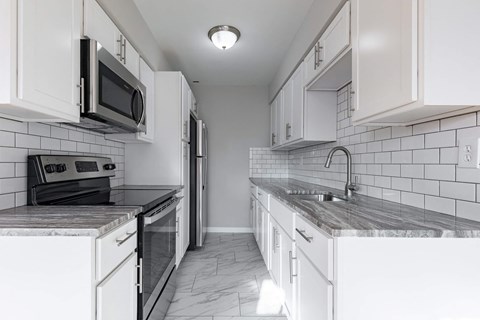 A kitchen with white cabinets and a black and white tiled backsplash.