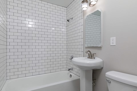 A white bathroom with a white tub, sink, and tiles.