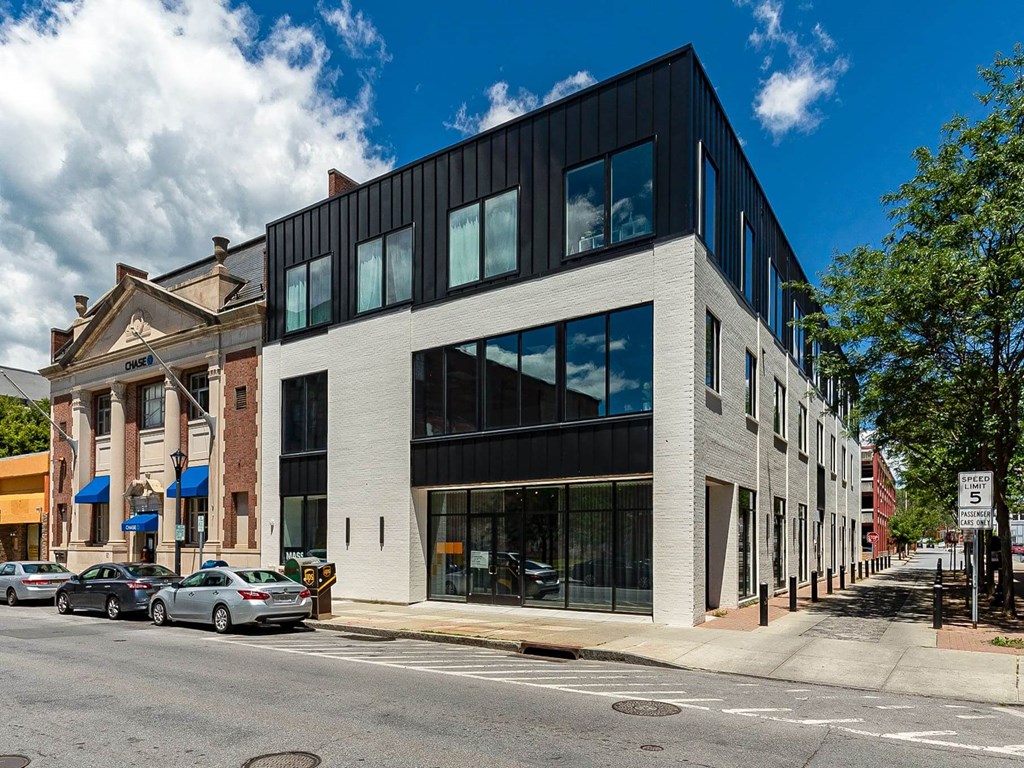 A modern building with a black and white facade is situated on a street corner with cars parked in front.