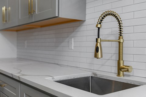 A kitchen sink with a gold faucet and a white countertop.