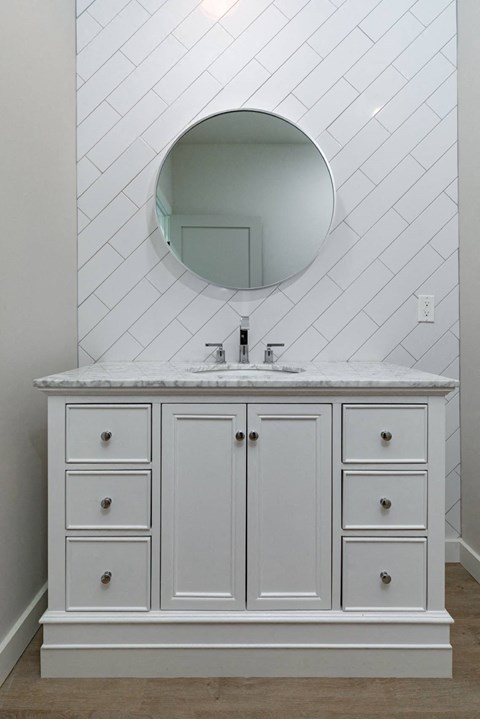 A bathroom vanity with a marble countertop and a round mirror above it.