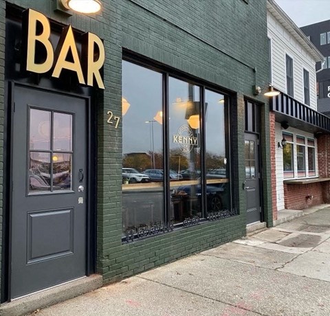 A bar with a black door and windows has a sign that says "Bar.".