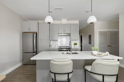 A modern kitchen with a white island and two chairs.