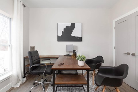 A black and white photo is hanging on a white wall above a black chair and a wooden table.