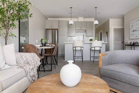 A living room with a grey couch, a wooden table, and a white vase on it.