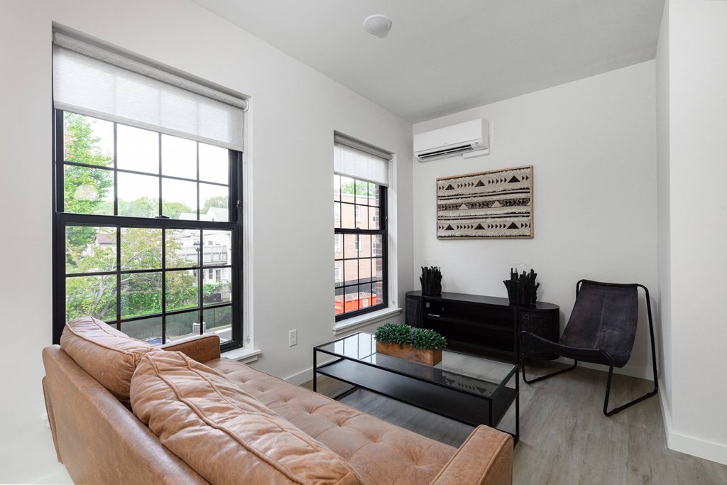 A living room with a brown couch, a black coffee table, and a window with a view of trees.