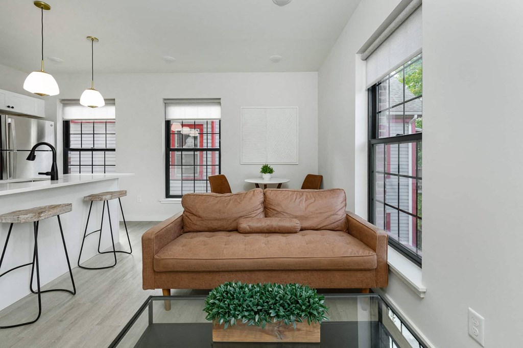A brown couch is in the middle of a white room with a glass table in front of it.