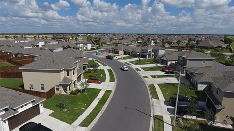 A residential street with houses on both sides and a car driving down the road.