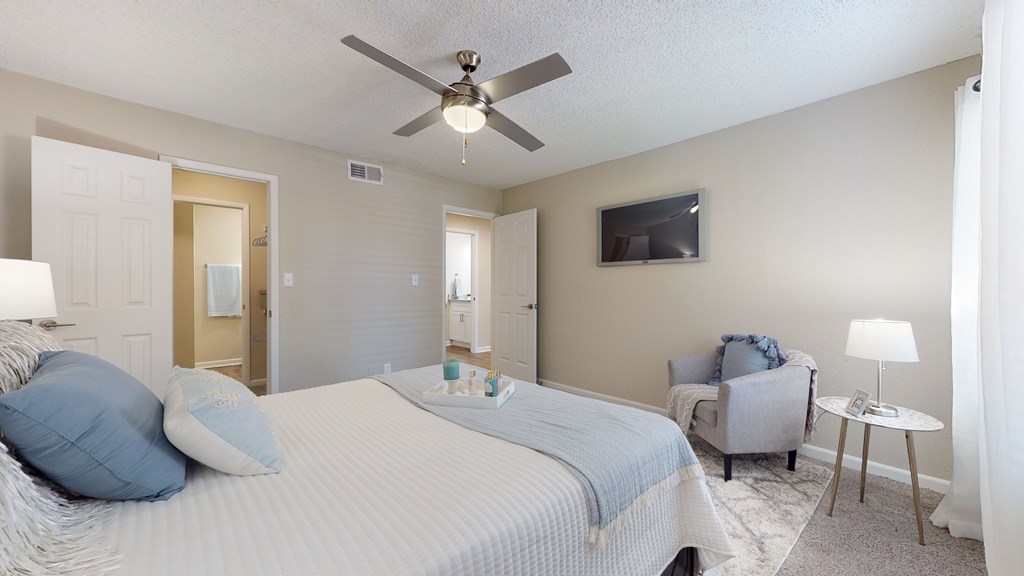 A bedroom with a bed, chair, and ceiling fan.