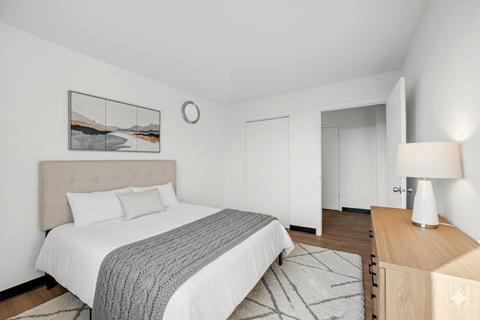 A bedroom with a large bed and a wooden nightstand at Fullerton Court Apartments, Chicago, IL