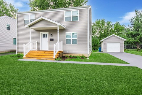 A house with a grey exterior and a white door is surrounded by a green lawn at Poplar Place Apartments, Springfield, IL 62703