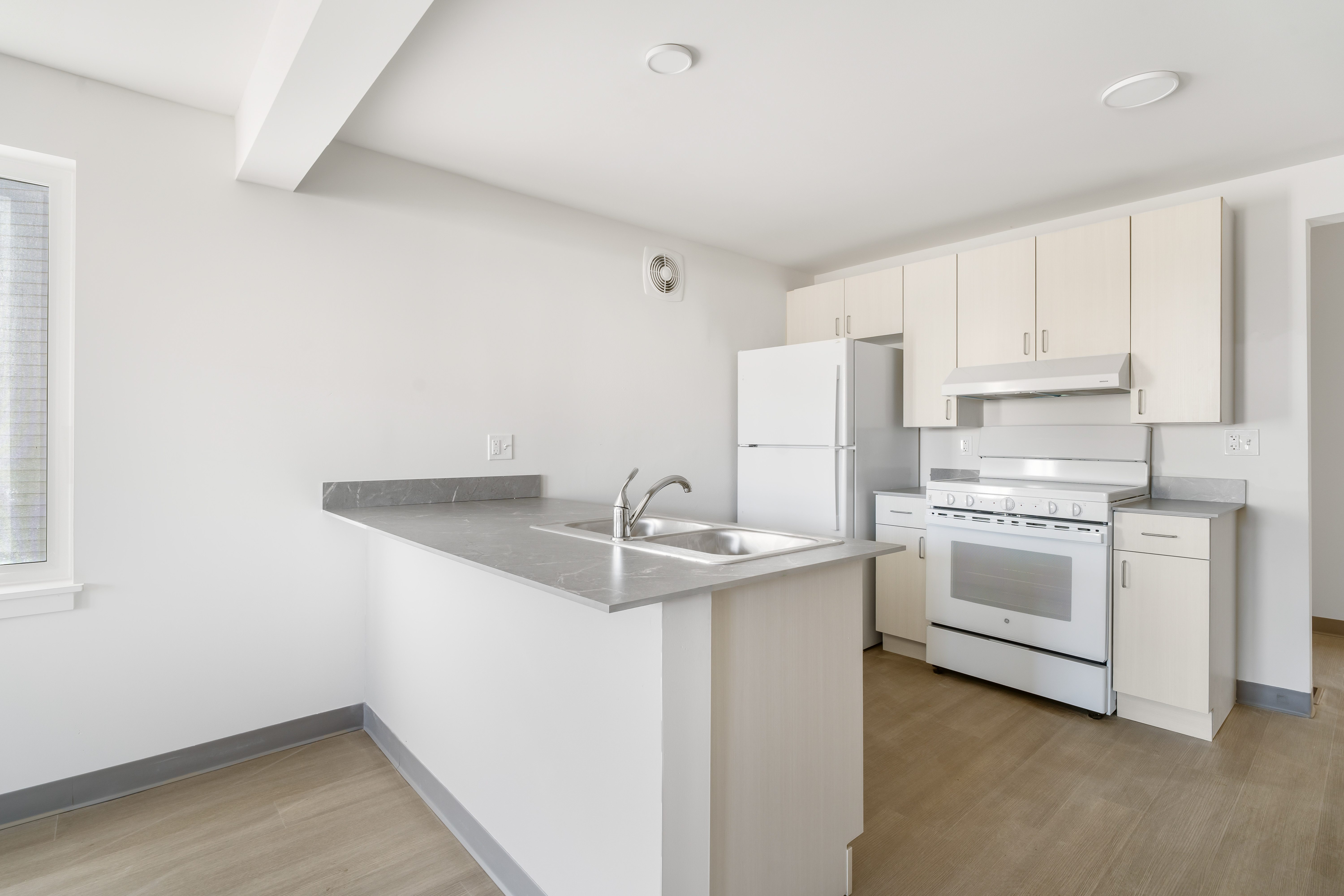 A kitchen with white appliances and wooden floors.
